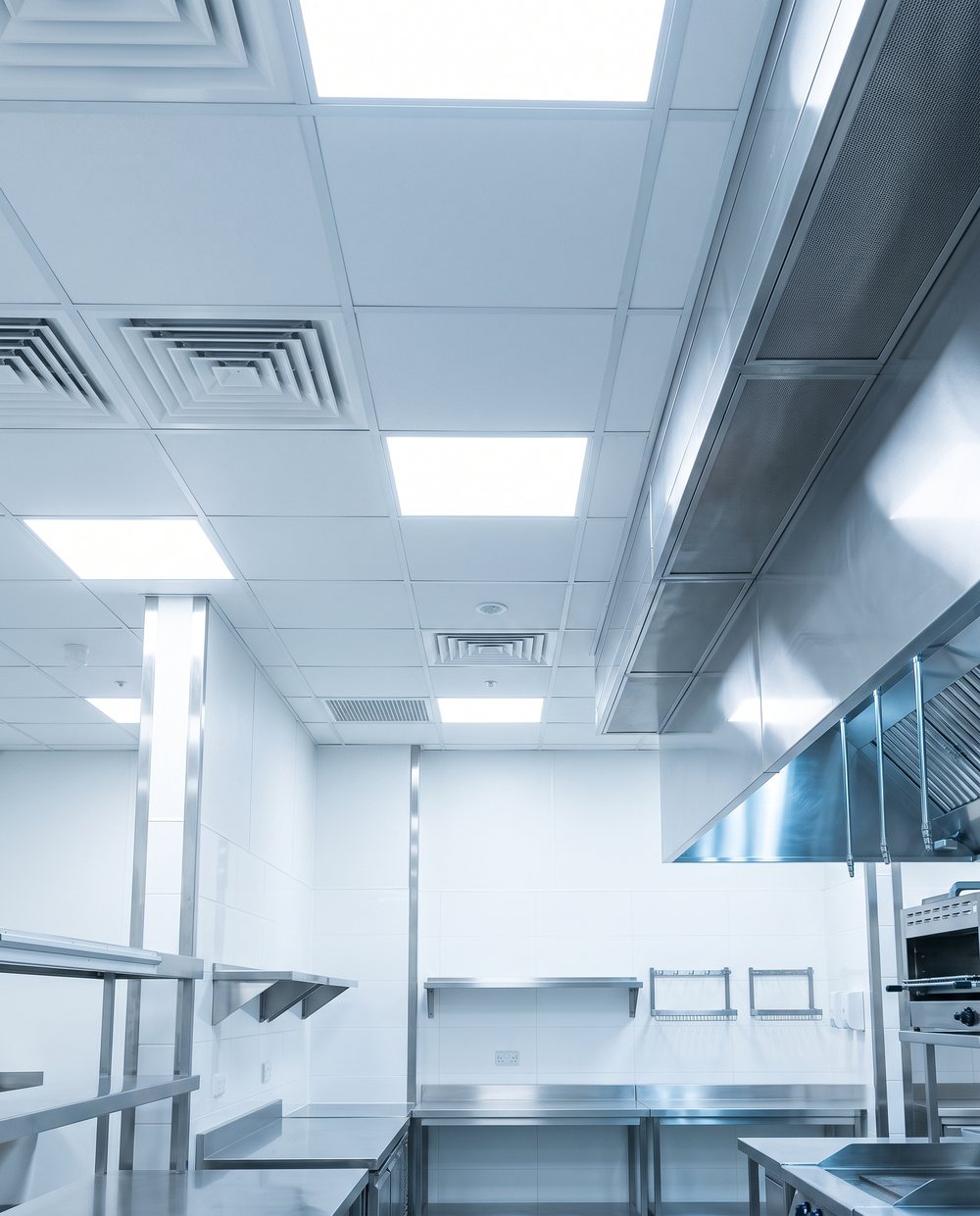 Spotless white acoustic ceiling tiles, clean ceiling vents and a polished stainless steel exhaust hood in a commercial restaurant kitchen in Edmonton